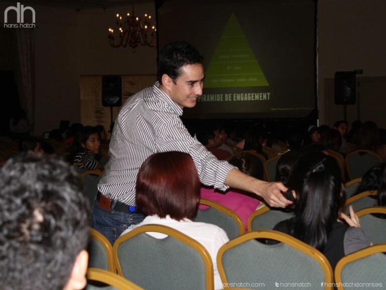 Un orador sonriendo y entregando un micrófono a un miembro de la audiencia en una sala de conferencias durante una presentación sobre marketing.