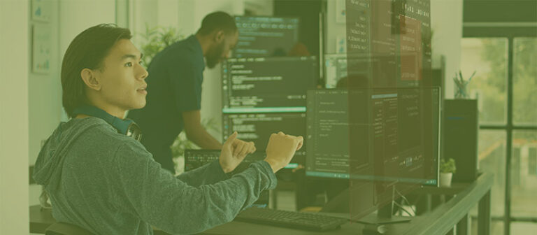 Un desarrollador de software que trabaja en varios monitores con software de codificación abierto en un entorno de oficina moderno.